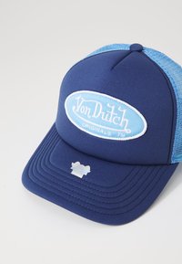 Casquette bleu marine avec des panneaux en maille bleu clair, une couronne arrondie, et un patch ovale proéminent affichant "Von Dutch Originals". Visière texturée.
