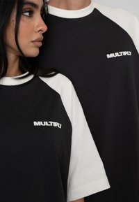 Černobílé raglánové trička s krátkým rukávem. Logo "MULTIPLY" v bílé barvě na černé části. Měkký, bavlněný materiál s kulatým výstřihem.