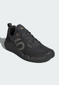 Černá sportovní bota s texturovaným svrškem, zpevněnou patou a gumovou podrážkou. Obsahuje decentní logo a zlaté akcenty na tkaničkách a jazyku.