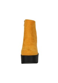 Botín de ante amarillo hasta el tobillo con una textura suave, punta redondeada, suela de plataforma negra y cremallera lateral para el cierre.