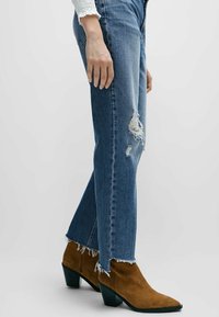Blå slitna jeans i denim med fransade fållar, kombinerat med bruna mockaankelstövlar med blockklack och spetsig tå.
