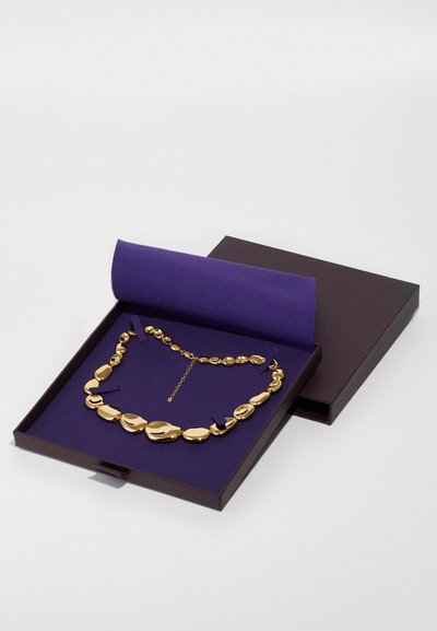 Collier en ton doré avec des formes ovales variées, présenté dans une boîte garnie de velours violet. Comprend une extension de chaîne pour une longueur adjustable.