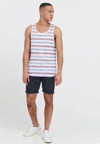 Canottiera a righe con tessuto blu, rosso e bianco; abbinata a pantaloni corti blu navy; modello che indossa sneaker bianche; superficie liscia, vestibilità casual.