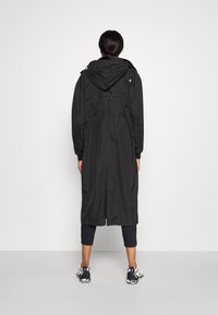 Abrigo largo negro con capucha, cintura ajustada y puños elásticos, con una textura suave y longitud hasta la mitad de la pantorrilla.