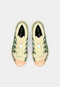 Αθλητικά παπούτσια με κορδόνια, με επάνω μέρος ανοιχτού κίτρινου χρώματος, πράσινες λεπτομέρειες και σόλα ροδακινί χρώματος. Υλικό από δίχτυ με υφή και σχέδια στην επιφάνεια.