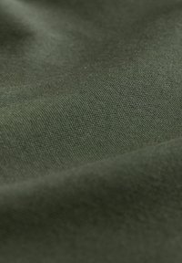 Žalia tekstilė su lygiu paviršiumi, turinčia tankų audinį ir subtilų blizgesį, kuriame matyti raukšlės ir raukšlės.