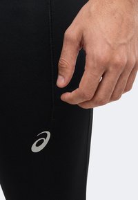 Gros plan d’une main reposant près de la couture et du logo sur un legging de sport noir.