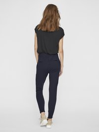 Black short-sleeve top paired with navy elastic waist joggers. Joggers feature a slim fit and two back pockets. Worn with beige sneakers.