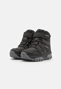 Black waterproof boots with a textured finish, featuring a velcro strap, laces, and a rugged gray rubber sole for traction.