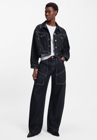 Tumša džinsa īss džinsa jaciņa ar redzamām šuvēm un divām priekšējām kabatām, kopā ar plaša piegriezuma tumša džinsa biksēm ar lielām sānu kabatām.