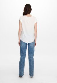 Vit kortärmad blus med rund halsringning och dragkedja bak, matchad med högmidjade ljusblå denimjeans med rak ben.