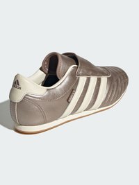Brown leather athletic shoe with white stripes and a velcro strap. Rounded toe, textured upper, and rubber outsole.