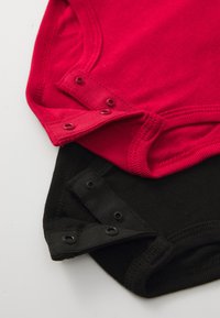 Two bodysuits, one red and one black, made of soft fabric. Each features snap closures at the bottom and ribbed edging.