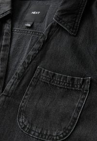 Schwarzes Denim-Hemd mit einem Button-Down-Kragen, Brusttasche und subtiler Textur. Etikett im Nacken sichtbar. Klassisches und vielseitiges Design.