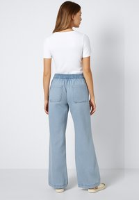 Jeans de tiro alto en azul claro, de pierna ancha, con cinturilla elástica y dos bolsillos traseros. Combinados con una camiseta blanca ajustada de manga corta.