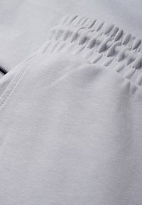 Jasnoszare spodnie dresowe wykonane z miękkiego, teksturowanego materiału, z elastycznym pasem i starannie przeszytymi szwami. Widok z bliska podkreśla szczegóły.