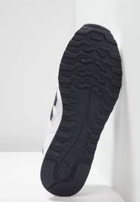 Schwarze Gummisohle mit Zickzackprofil, ausgestattet mit einem weißen Obermaterial und einem Designelement in Marineblau. Insgesamt glatte Textur.