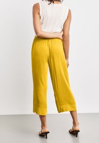 Żółte, krótki spodnie wykonane z gładkiego materiału z plisowaną talią i bocznymi rozcięciami na dole. Noszone z fakturowaną białą bluzką.