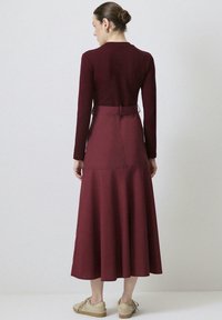 Burgundy långärmad klänning med en åtsittande bodice och utsvängd, lager-på-lager kjol. Mjuk tyg med cinched midja och bakdetaljer. Avslappnade skor.