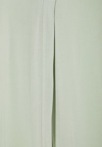 Tissu vert clair à texture lisse avec des plis verticaux. Un éclat subtil et un tombé doux rehaussent l'apparence générale.