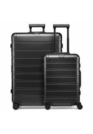 Dos maletas negras de carcasa dura con asas telescópicas y cuatro ruedas, una grande y otra más pequeña, situadas lado a lado sobre fondo blanco.