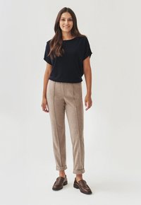 Marineblauw T-shirt met korte mouwen, beige op maat gemaakte broek met zijs inzetten, en bruine instappers, staand tegen een lichte achtergrond.