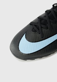 Svart fotbollssko med en strukturerad ovandel, svarta snören och en framträdande blå swoosh-logotyp längs sidan. Utformad för prestanda.