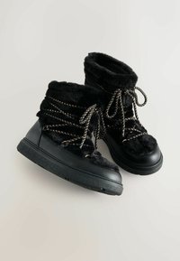 Schwarze Kunstfell- und Gummistiefel mit silberner Schnürung und strukturiertem Sohlenprofil. Runde Zehenpartie und weicher, gepolsterter Kragen für zusätzlichen Komfort.