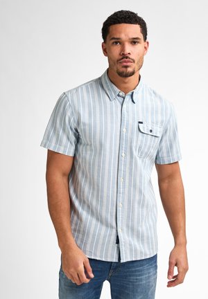 Kurzarmhemd in Hellblau mit vertikalen weißen Streifen. Mit einem Button-Down-Kragen und einer Brusttasche. Getragen mit blauen Jeans.