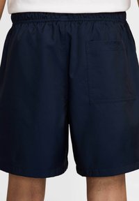 Granatowe szorty z elastycznym pasem, tylną kieszenią oraz gładkim, lekkim materiałem. Ogolnie wykończone, bez widocznych wzorów lub elementów metalowych.