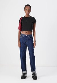 Black cropped t-shirt, blue high-waisted jeans with cuffed hems, and black platform shoes. A burgundy handbag is slung on the shoulder.