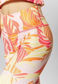 Legginsy z wysokim stanem w tropikalny wzór liści, w odcieniach pomarańczowym, różowym i żółtym. Wykonane z gładkiego, elastycznego materiału z dekoracyjnym przeszyciem.