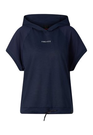 Kvinde står iført navyblå kortærmet hættetrøje, matchende vidde bukser, sorte sko og en bagvendt navyblå baseballkasket.