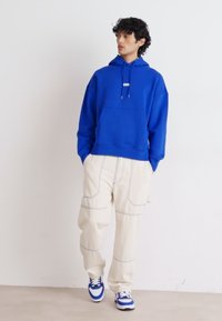 Kongelig blå hettegenser med frontlomme, parret med kremfargede cargo-bukser med blå søm, og sneakers med blå aksenter.