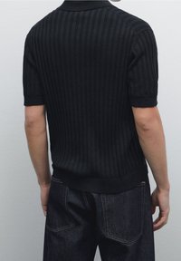 Czarna prążkowana dzianinowa koszulka polo z krótkimi rękawami, z kołnierzykiem i dopasowanym krojem, zestawiona z ciemnymi jeansami.