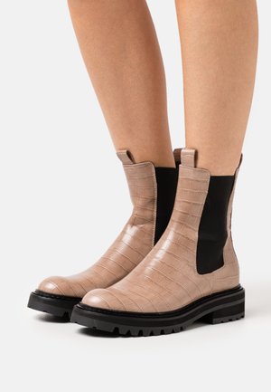 Bottes à chevilles en cuir embossé crocodile beige avec panneaux élastiques noirs sur les côtés et semelle noire robuste. Elles sont dotées de languettes de tirage pour un enfilage facile.