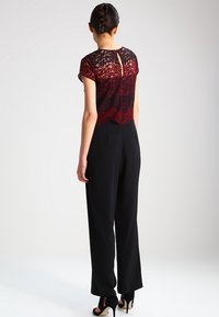 Bordeaux kanten top met een keyhole achterkant, gecombineerd met strakke zwarte broek met een ontspannen pasvorm en een gladde textuur.