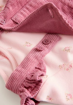 Completo per bebé di un delicato rosa pallido caratterizzato da un design floreale con morbidi volant e bottoni di una tonalità rosa più intensa, ripiegato ordinatamente su uno sfondo bianco.