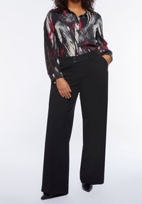 Pantaloni neri a gamba larga abbinati a una camicia a maniche lunghe con bottoni, dai colori nero, rosso e bianco, caratterizzata da un motivo astratto e dalla vestibilità rilassata.