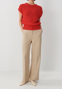 Czerwony sweter na krótki rękawek z dzianiny o fakturowanym wzorze; zestawiony z beżowymi spodniami z wysokim stanem; kremowe buty na spiczastym obcasie.