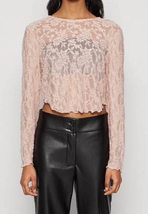 Top corto a maniche lunghe in pizzo floreale trasparente di un delicato rosa chiaro, con bordi ondulati. Abbinato a pantaloni in pelle neri a vita alta con dettagli in bottoni.