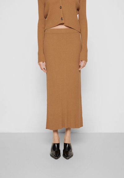 Conjunto de suéter canelado castanho, com mangas longas e uma bainha cropped, combinado com uma saia até ao joelho e sapatos de salto agudo pretos.
