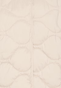 Doudoune matelassée beige clair avec un motif ondulé, une texture lisse et une fermeture éclair centrale. Tissu doux offrant chaleur et confort.
