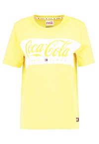 Żółta bawełniana koszulka z krótkim rękawem, ozdobiona białym i żółtym logo Coca-Cola oraz napisem "Tommy Jeans". Okrągły dekolt.