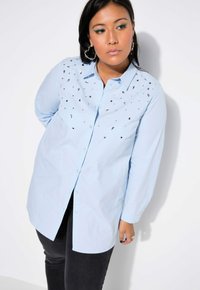 Camicia azzurro chiaro con bottone, caratterizzata da piccole decorazioni in argento sparse sulla parte anteriore, maniche lunghe e una vestibilità rilassata.