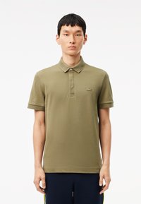 Polo shirt verde oliva realizzato in tessuto morbido, dotato di un colletto classico, maniche corte e un piccolo logo ricamato sul petto.