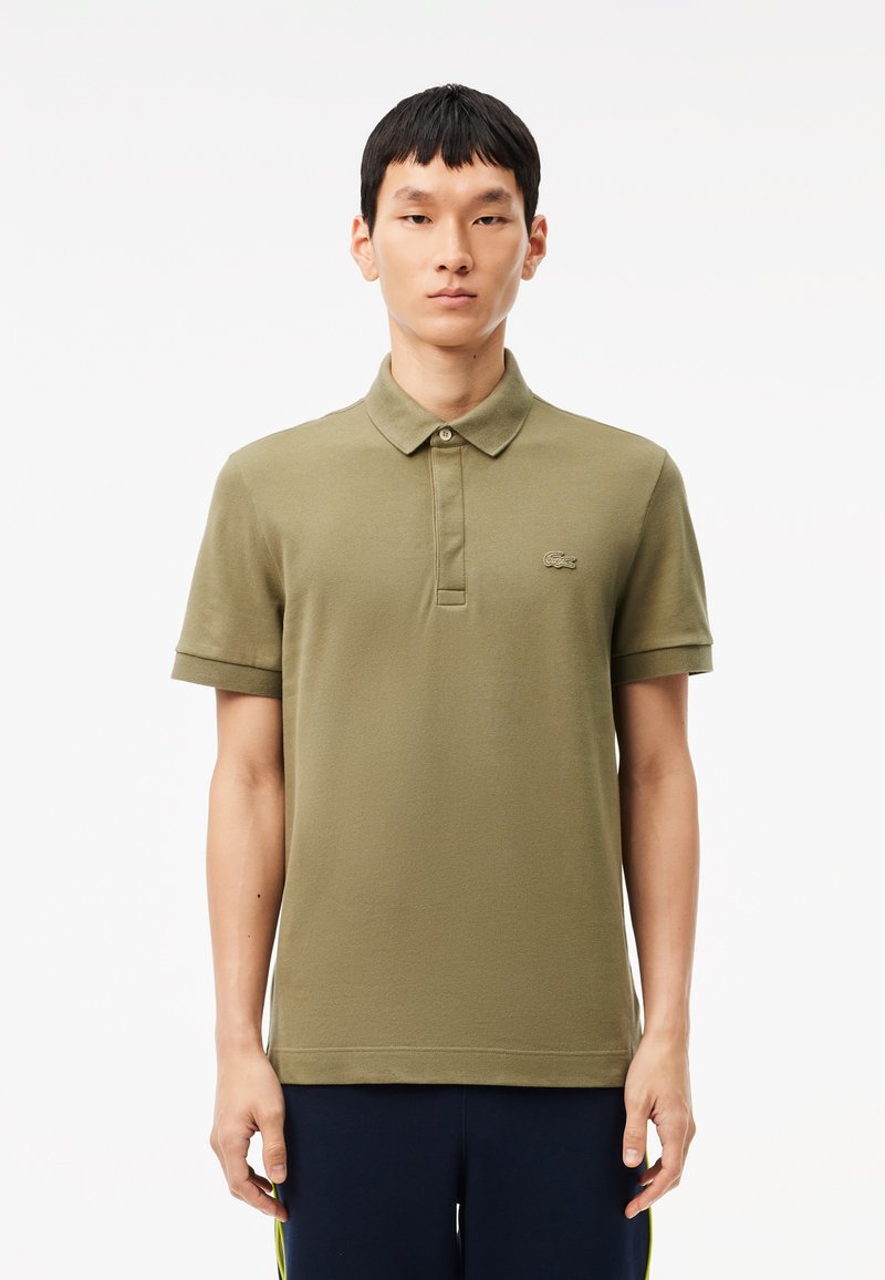Polo shirt verde oliva realizzato in tessuto morbido, dotato di un colletto classico, maniche corte e un piccolo logo ricamato sul petto.