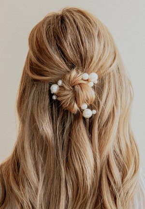Accessorio per capelli composto da capelli biondi attorcigliati con perle decorative di varie dimensioni. Texture liscia, tonalità neutre e design elegante.