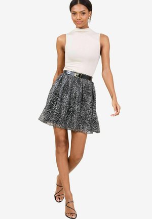 Black and white patterned skirt with a flared design, paired with a light beige sleeveless top and a black belt. Thin black strappy sandals.