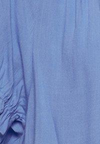 Jasnoniebieska tkanina o gładkiej fakturze, z marszczonymi detalami z jednej strony i lekko pomarszczonym wykończeniem.
